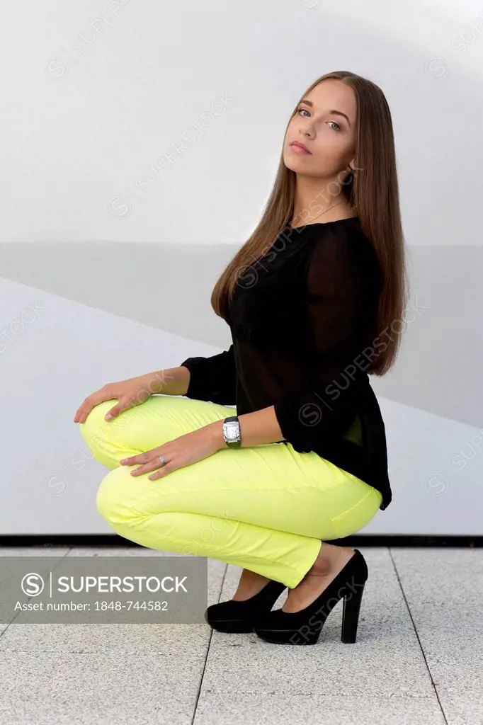 Young woman with a black top, bright yellow trousers and black high heels