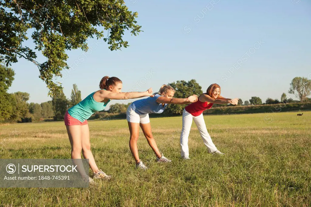 Three young women doing gymnastics exercises together in a meadow