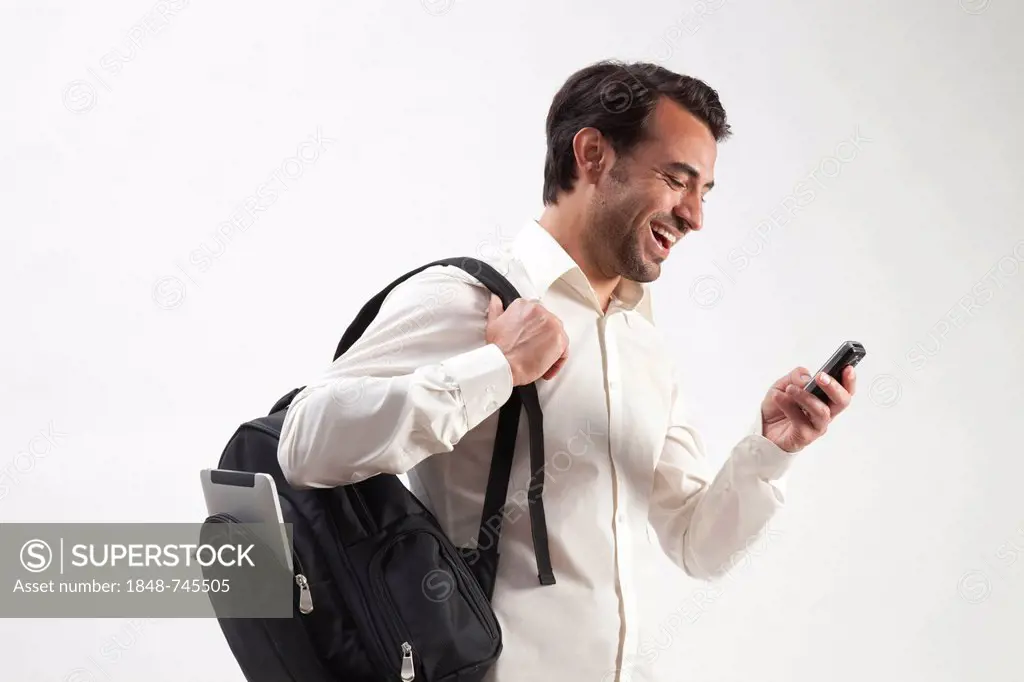 Smiling man wearing a backpack, from which an iPad is sticking out, talking on a mobile phone