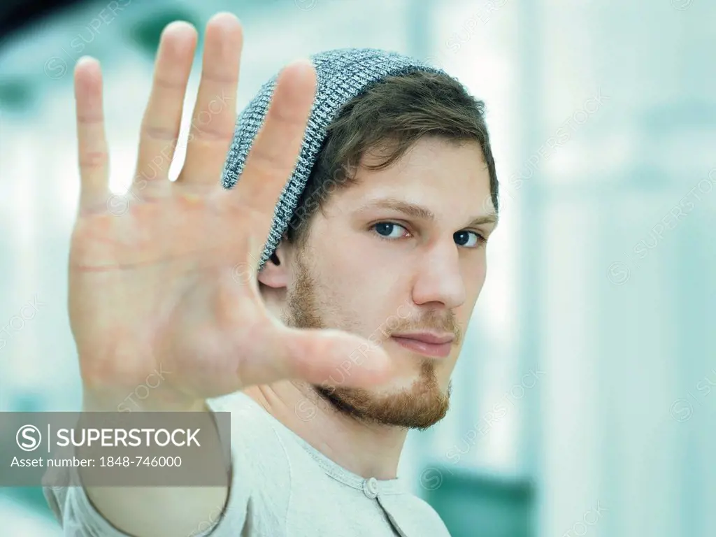 Portrait of a young man with a bear with a woolly hat, defensive gesture, irritated