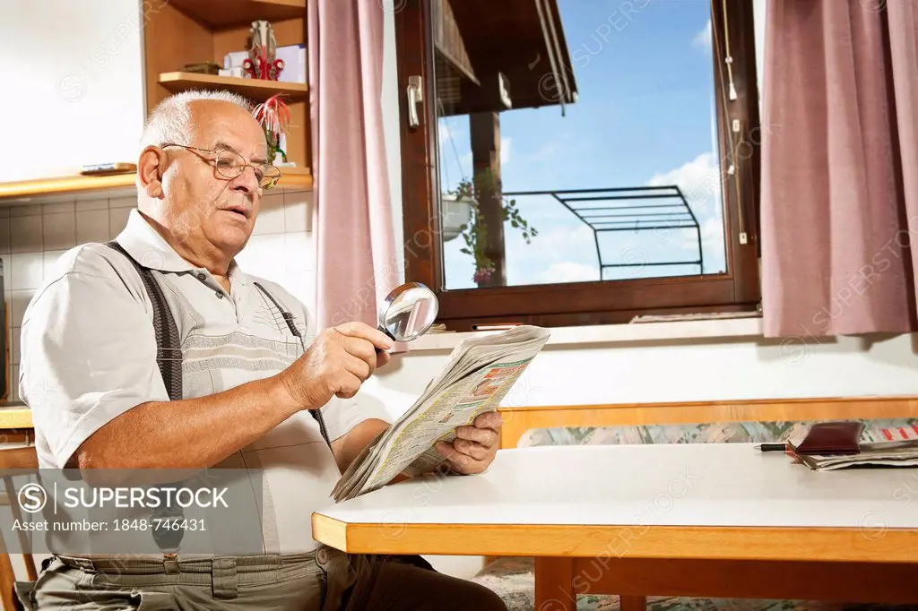 Elderly man reading a newspaper with a magnifying glass