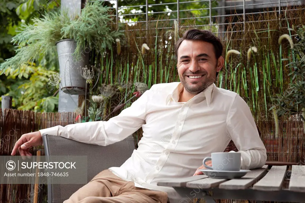 Smiling man sitting with a coffee cup on the balcony