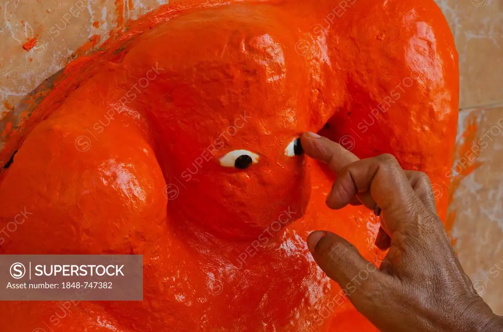 Sculpture of God Ganesha getting freshly painted with orange paint, Varanasi, India, Asia