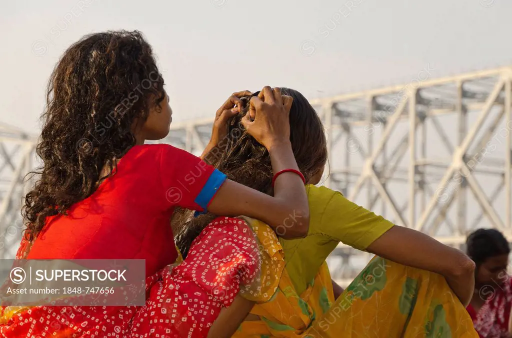 Youg woman looking for lice in the hair of another woman, in front of Howrah Bridge, Kolkata, India, Asia