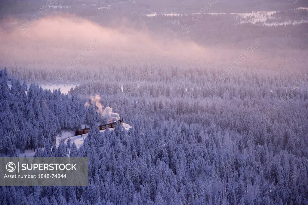 View from the Brocken mountain over a winter landscape deeply covered in snow at sunset and the Harzer Schmalspurbahn, narrow-gauge railway with steam...