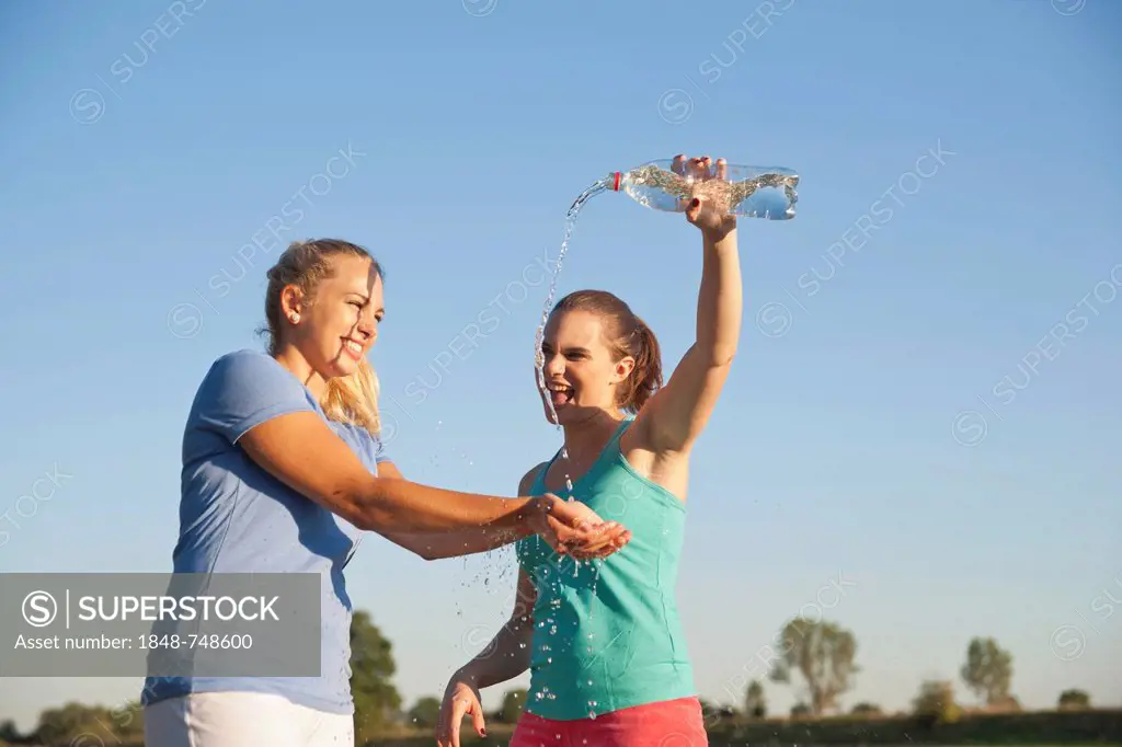 Two young women having fun with a bottle of water during a drink break while doing sports