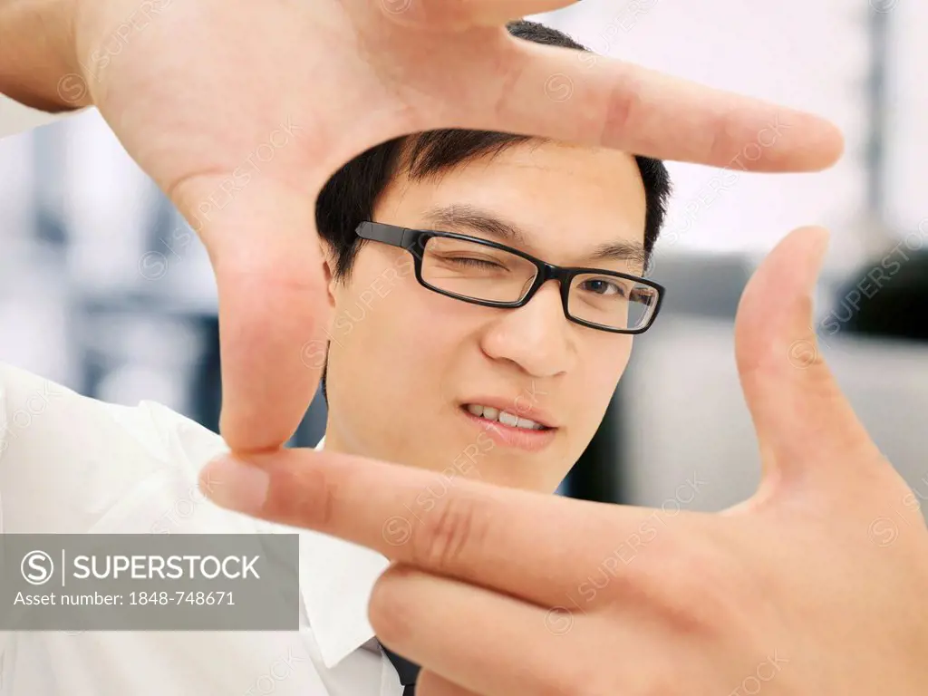 Young businessman, Asian, with glases, friendly, holding fingers as a rectangle shape in front of face, gesture