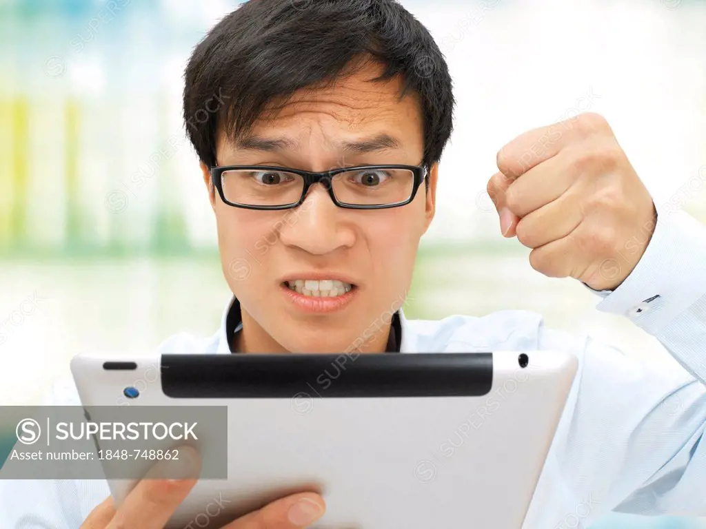 Young businessman, Asian, with glasses, iPad, hand clenched in a fist, upset, angry, stressed out