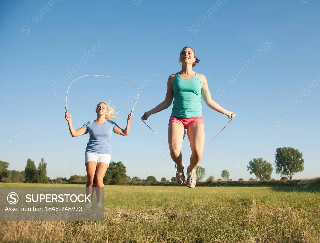 Two young women jumping rope in a meadow
