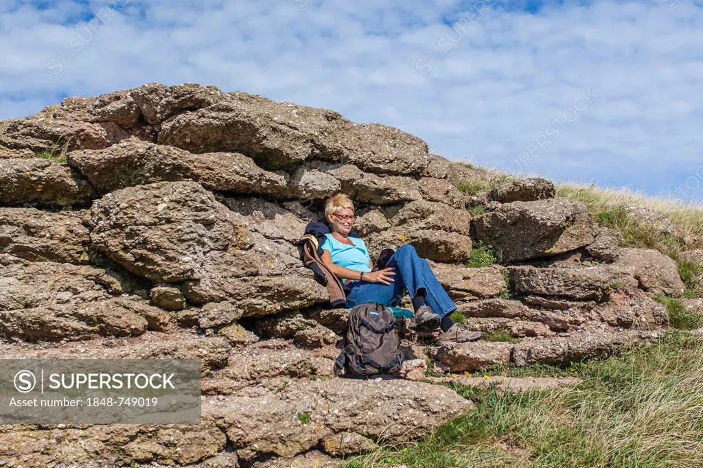 Woman sitting in front of a rock and reading a book, island of Heligoland, Schleswig-Holstein, Germany, Europe