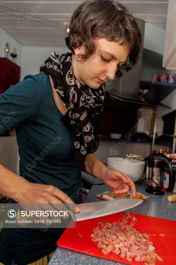 Girl, 14 years old, cutting ham in a kitchen with a knife