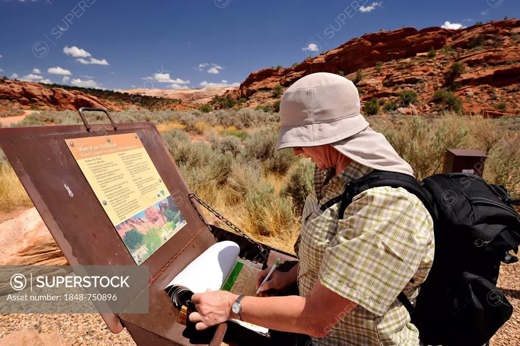 Tourist with a sun shield signing the registration box at Trailhead Wirepass, starting point to The Wave Navajo sandstone rocks, North Coyote Buttes, ...