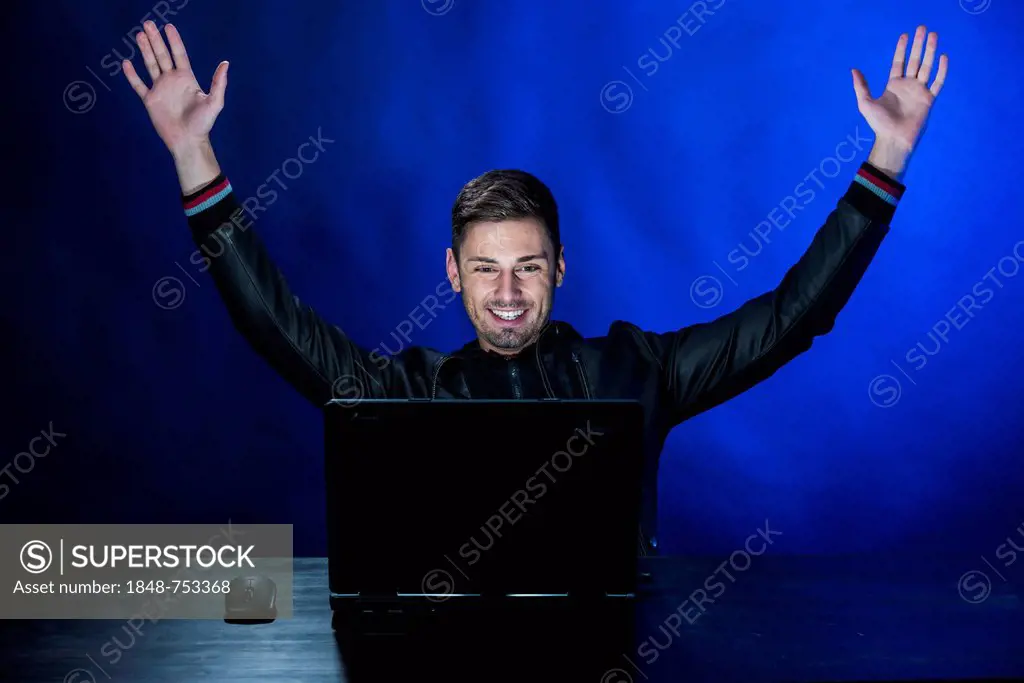 Young man sitting in the dark in front of a laptop, with a joyful expression, exulting