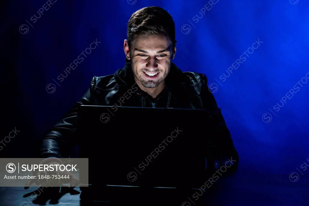 Young man sitting in the dark in front of a laptop, with a joyful expression