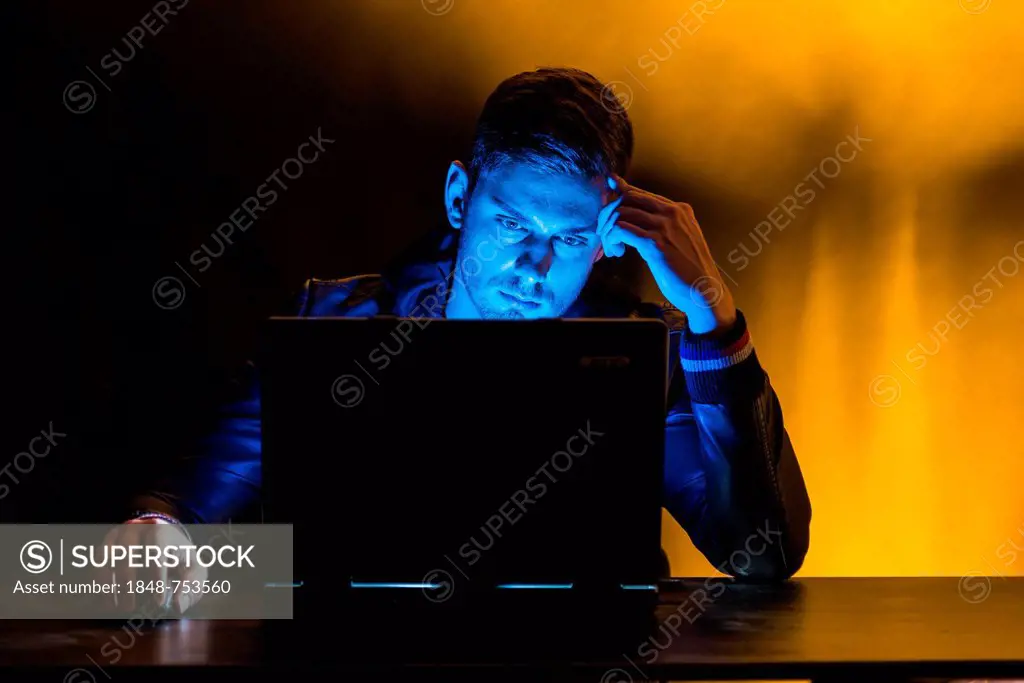 Young man sitting in the dark in front of a laptop