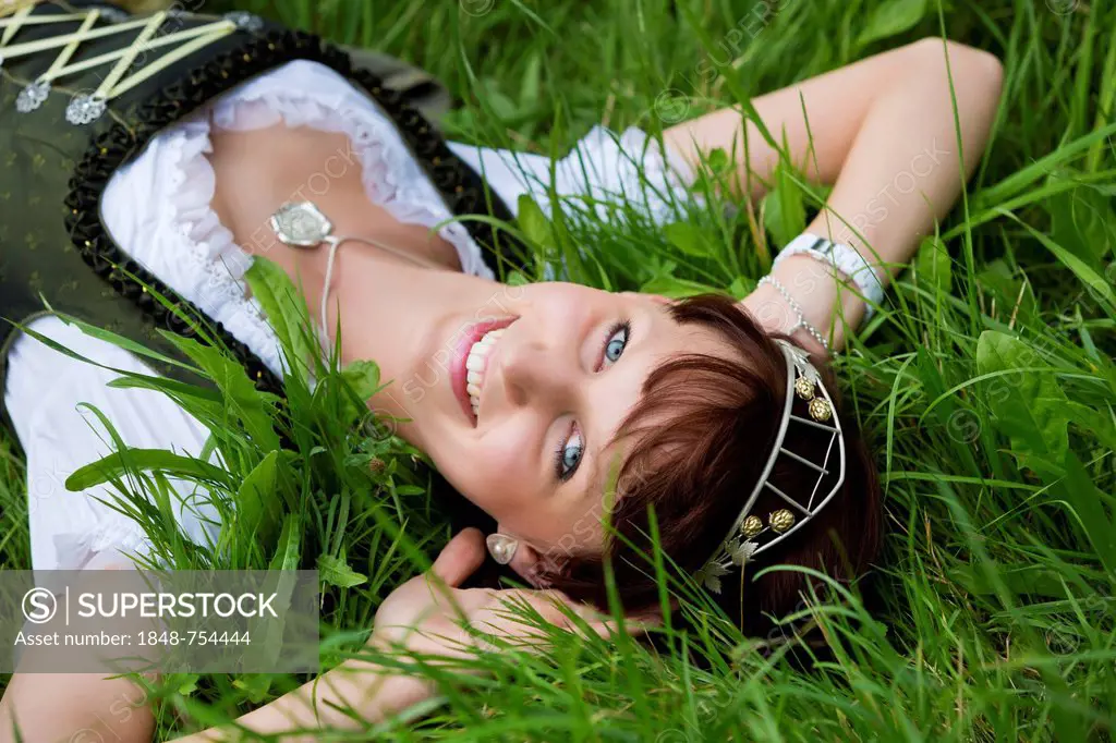 Young woman in a dirndl with a hop crown, lying in the grass, Hop Vicequeen of Hallertau, Holledau or Hollerdau, Bavaria, Germany, Europe