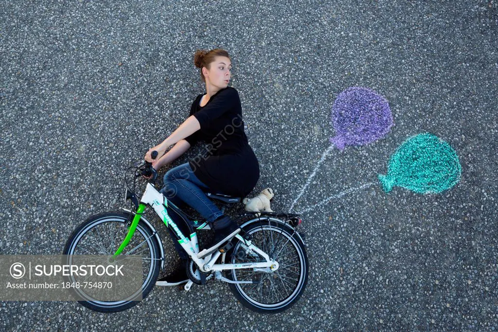 Young woman appearing to cycle on a children's bicycle, painted balloons tied to the rack, taken from above