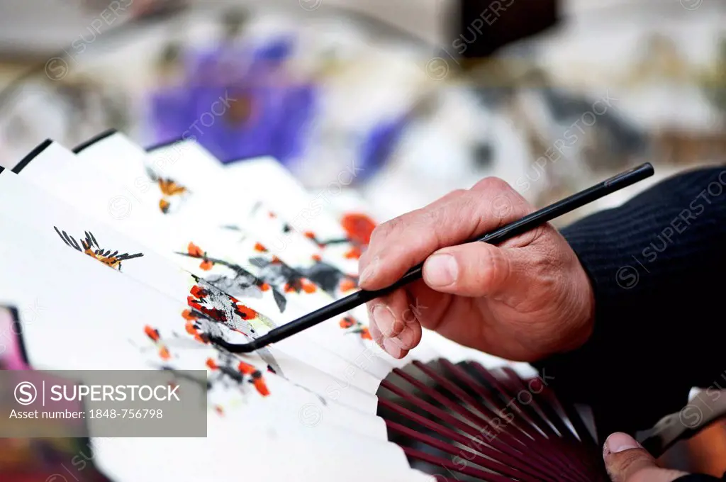 Close-up of a man painting a traditional design on a paper fan at a street market in Seoul, South Korea, Asia