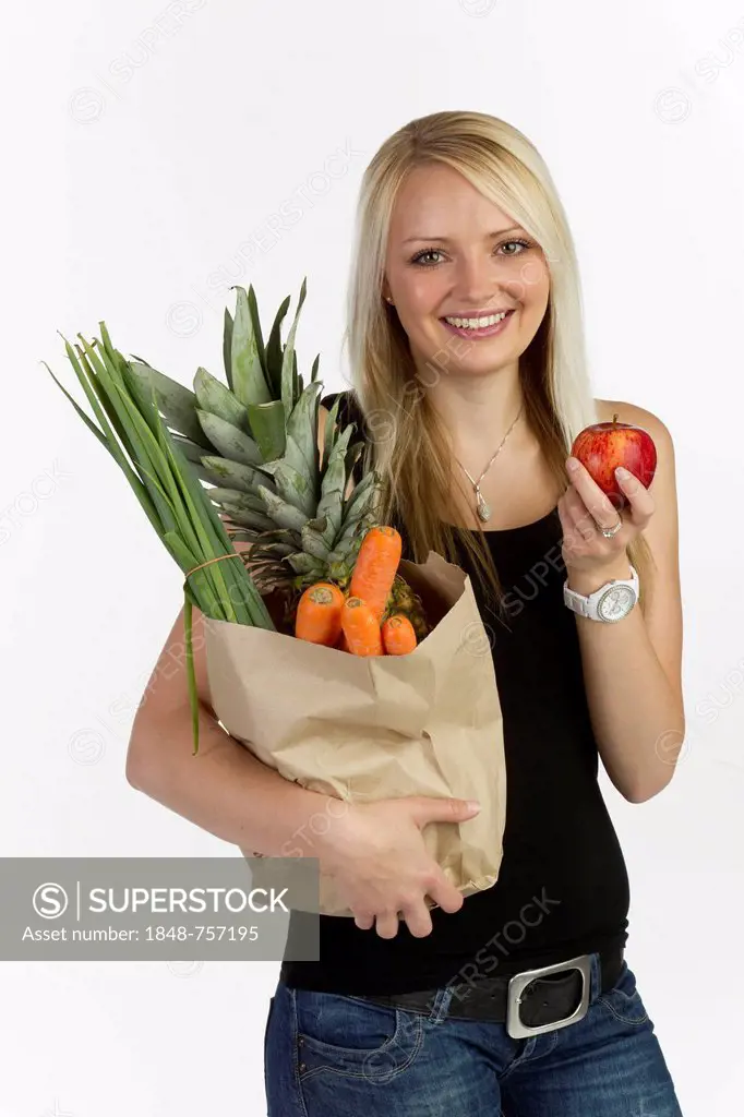 Young woman with a bag full of vegetables and fruit in her arm, holding an apple in her hand