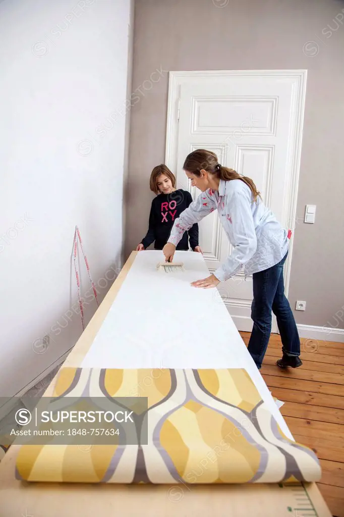 Mother and daughter renovating a room, preparing wallpaper for wallpapering a wall