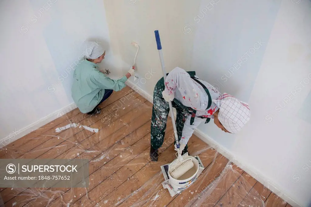 Mother and daughter renovating a room, painting the walls with paint rollers