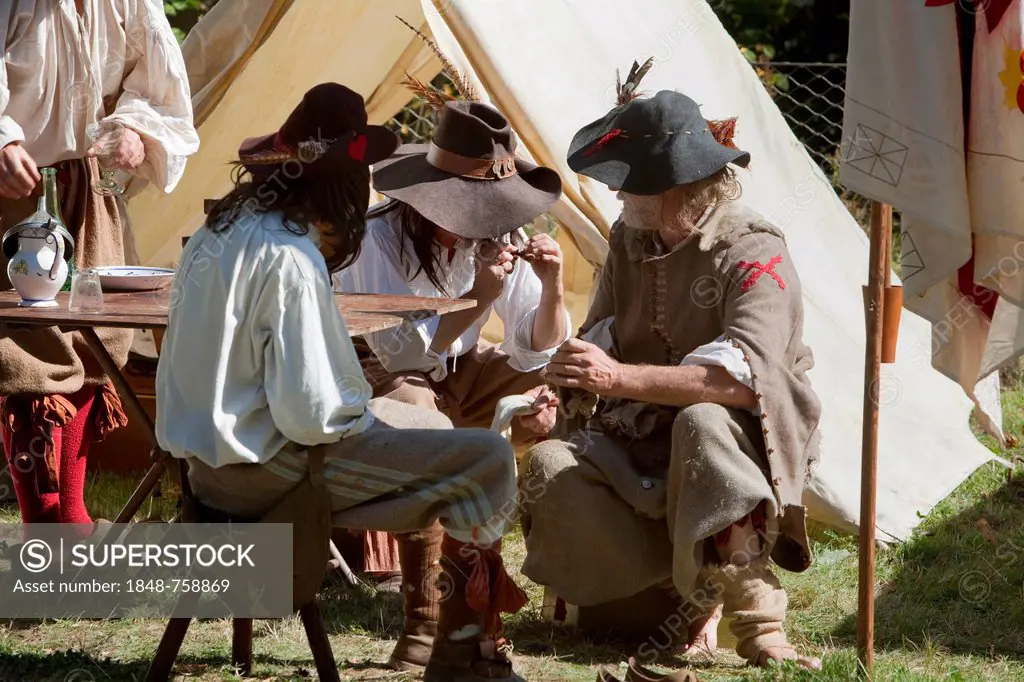 Men dressed in Medieval costumes sitting in front of a tent, live role-playing or ReenLarpment, historical reconstruction by a reenactment group, in f...