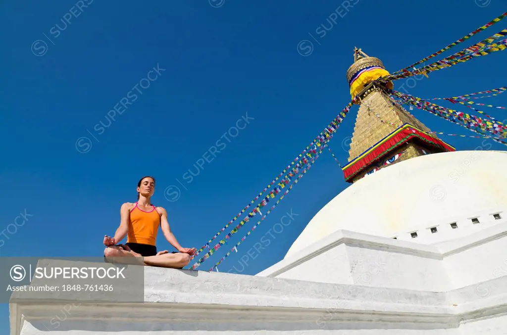 Young woman practicing yoga at the Boudhanath stupa, showing the Padmasana pose, or Lotus pose
