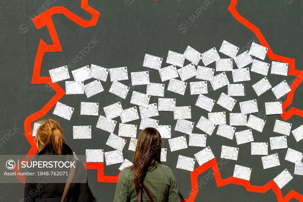 Two young female tourists standing in front of a wall with postcards, display set up for the 775th anniversary celebrations of the city of Berlin, at ...
