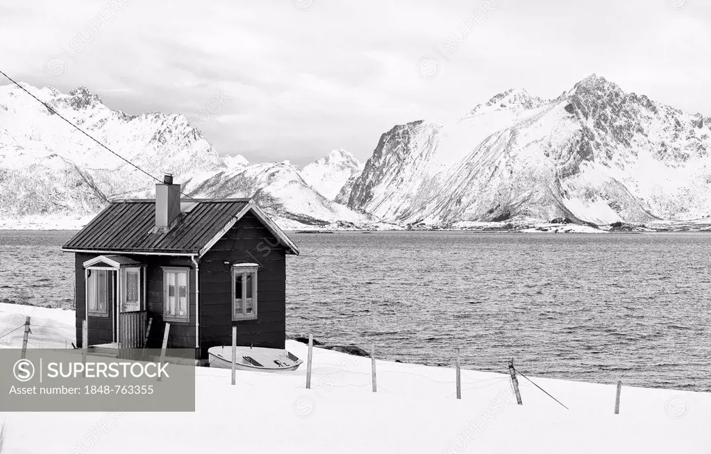 Black and white image of a secluded fisherman's house on a winter fjord in the Lofoten Islands in northern Norway, Moskenesoeya, Lofoten, Nordland, No...