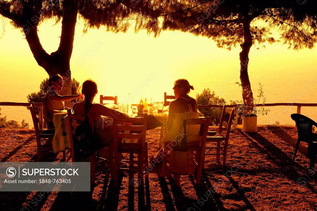 Three women sitting at a table at sunset, evening mood in a Greek seaside garden, Lefkas or Lefkada, Greece, Europe