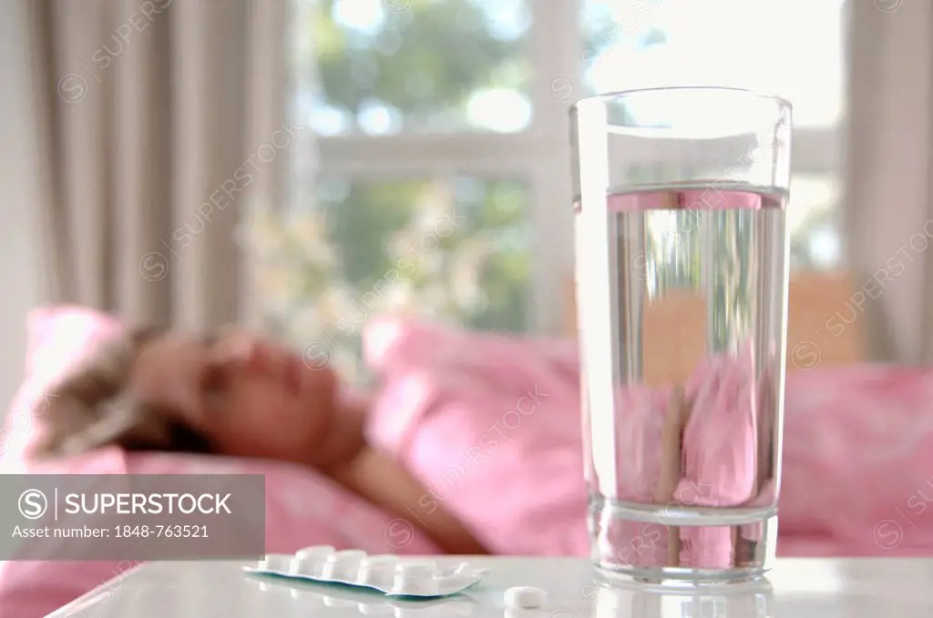 Glass of water with tablets, woman lying in bed at back