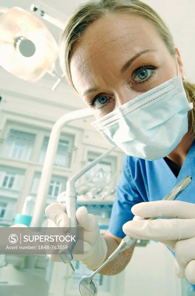 Dentist, dental hygienist, wearing a face mask in a treatment centre while holding a mirror and a drill