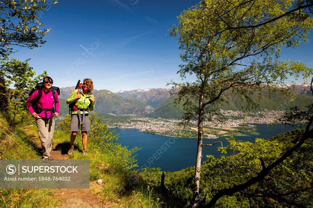 Two women hiking on the high trail of Monti di Vairano to Monti Caviano on Monte Gambarogno, overlooking the Maggia delta, Ascona and Locarno, Ticino,...