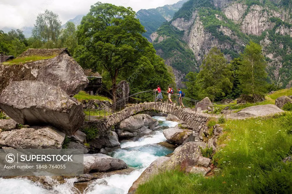 Three hikers crossing a medieval arch bridge, Puntid, Val Calneggia, Bavona Valley, Valle Maggia, Ticino, Switzerland, Europe