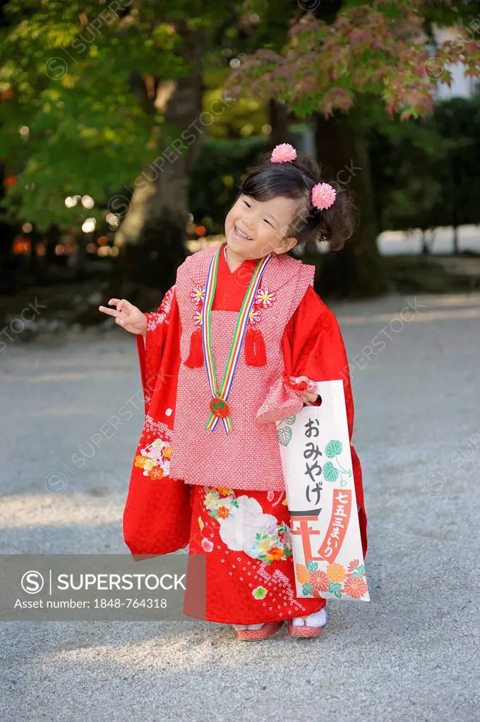 Shichi-go-san, Seven-Five-Three festival, girl in a red kimono holding a long bag with candy canes, Chitose-ame, standing on the gravel at the Shimoga...