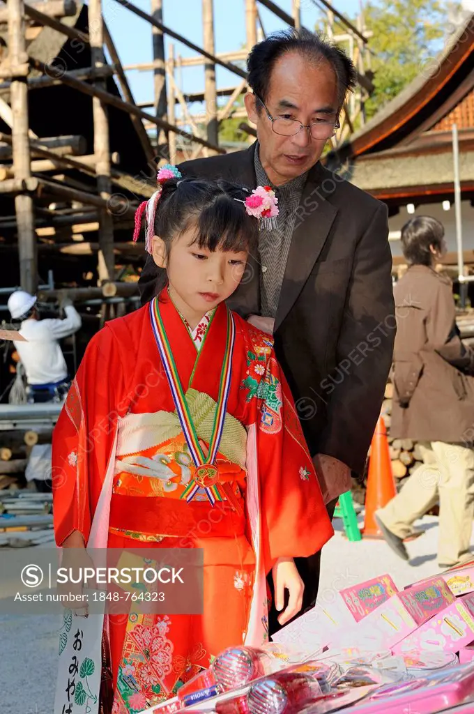 Shichi-go-san, Seven-Five-Three festival, a father and his daughter in a red kimono who is holding a long bag with candy canes, Chitose-ame, are selec...