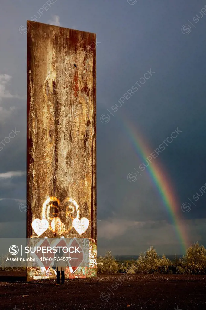 Man standing in front of the steel slab on Schurenbachhalde, a former spoil tip, with a rainbow, Essen, North Rhine-Westphalia, Germany, Europe, Publi...