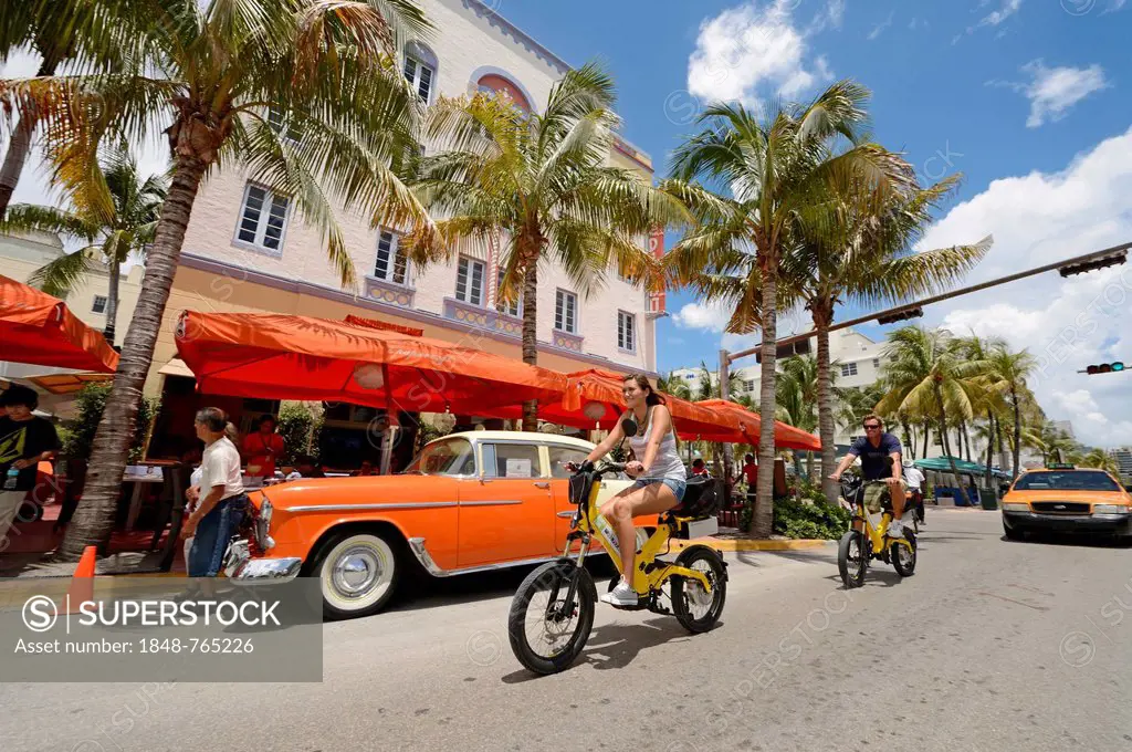 Couple riding electric bicycles, Ocean Drive, South Beach, Miami, Florida, USA