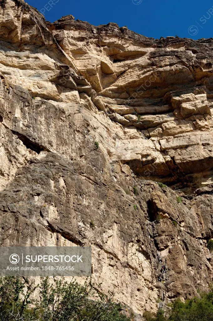 Rock face at the western flank of the Grand Canyon of Oman in the Wadi at Nakhar with hikers on the fixed climbing route leading to the exit from the ...