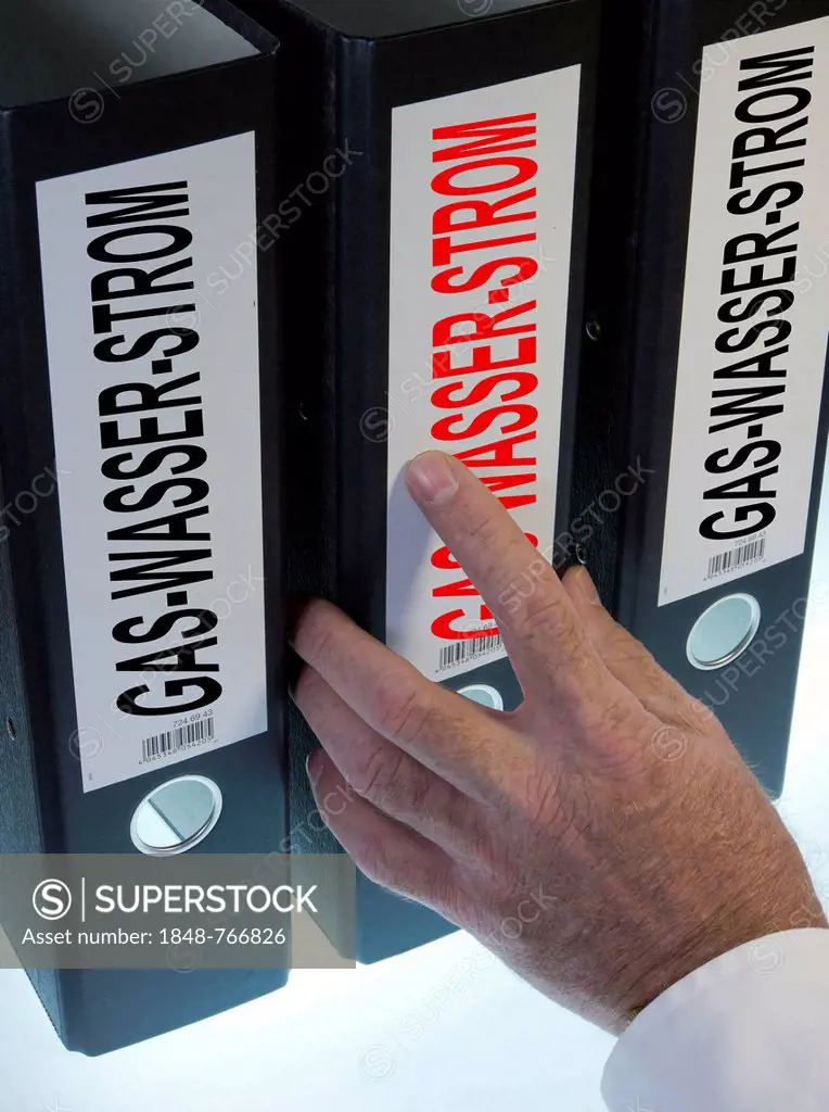 Hand reaching for a ring binder labeled Gas-Wasser-Strom, German for gas-water-electricity, symbolic image