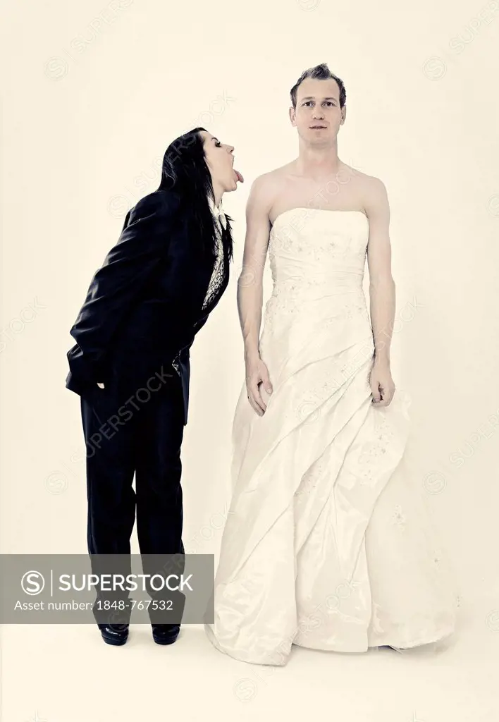 Bride wearing a suit poking her tongue out at the groom wearing a wedding dress, exchange of wedding clothing