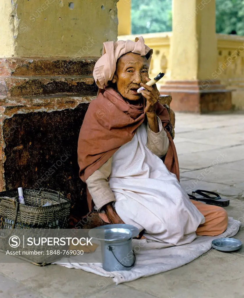 Elderly Burmese woman smoking a Cheerot cigar and wearing a headscarf, beggar