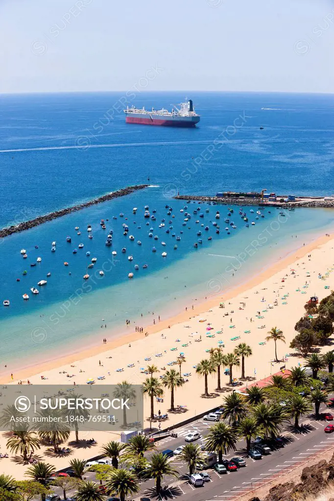 The sandy beach of Playa de las Teresitas with palm trees, large container ship at back, bird's eye view