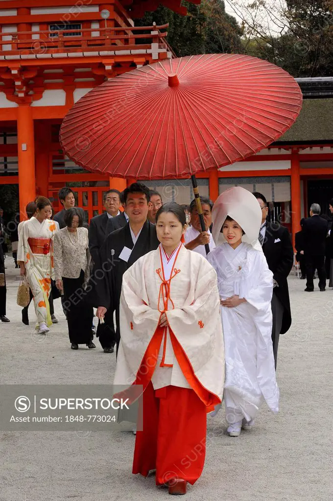 Japanese woman wearing scarlet hakama pants and a white kimono shirt with lengthy sleeves, in front of the gatehouse of Shimogamo Shrine
