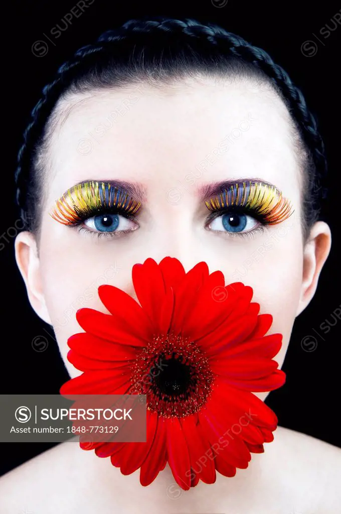 Young woman with colourful eyelashes and a red flower in her mouth