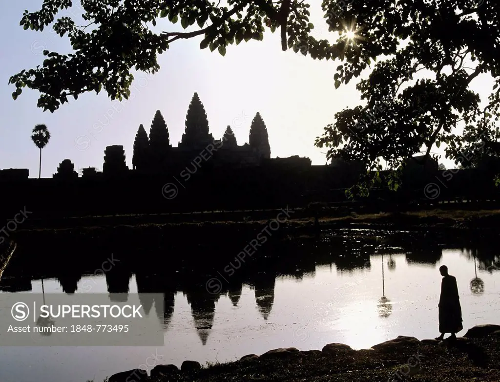 Main temple of Angkor Wat reflected in a pond with a monk standing at the shore, silhouette at sunrise, UNESCO World Cultural Heritage Site