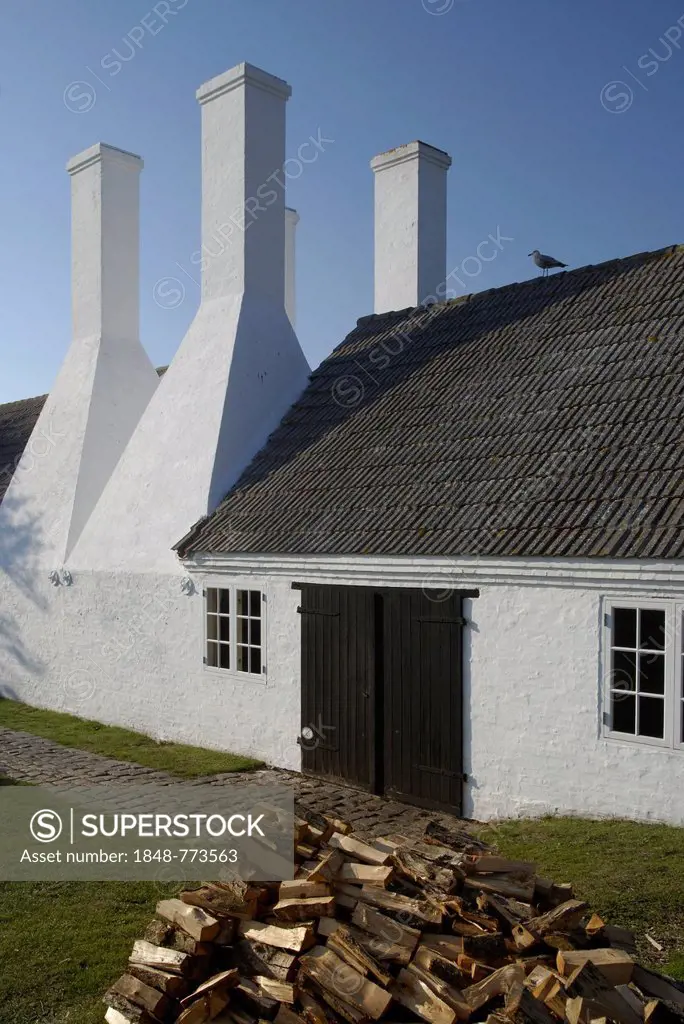 Four chimneys of a Bornholm herring smokehouse, stack of alder wood at the front