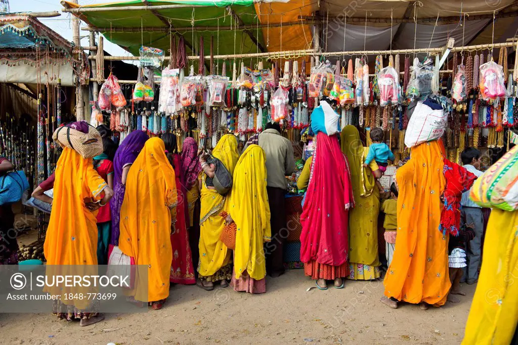 Indian women in colorful saris standing in front of a stall selling toys and fashion jewellery, Pushkar Camel Fair