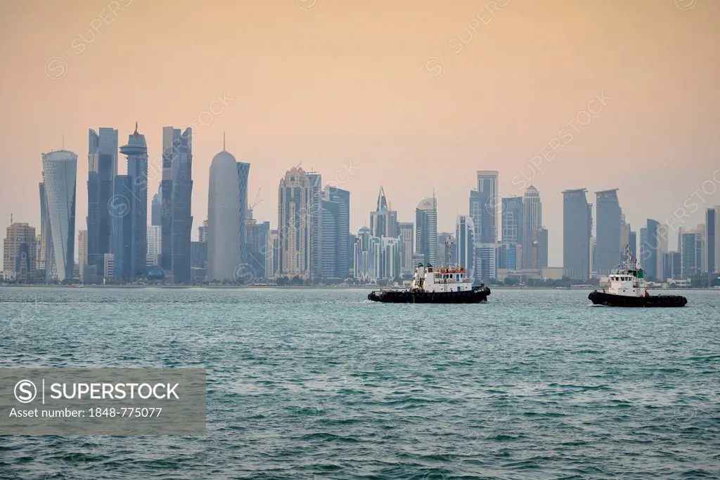 Tugboats in front of the skyline of Doha at dusk