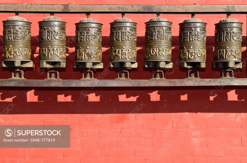 Buddhist prayer wheels in front of a red wall at Swayambhunath Stupa, Monkey Temple